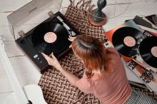 Woman placing a vinyl record on a turntable, next to a record collection